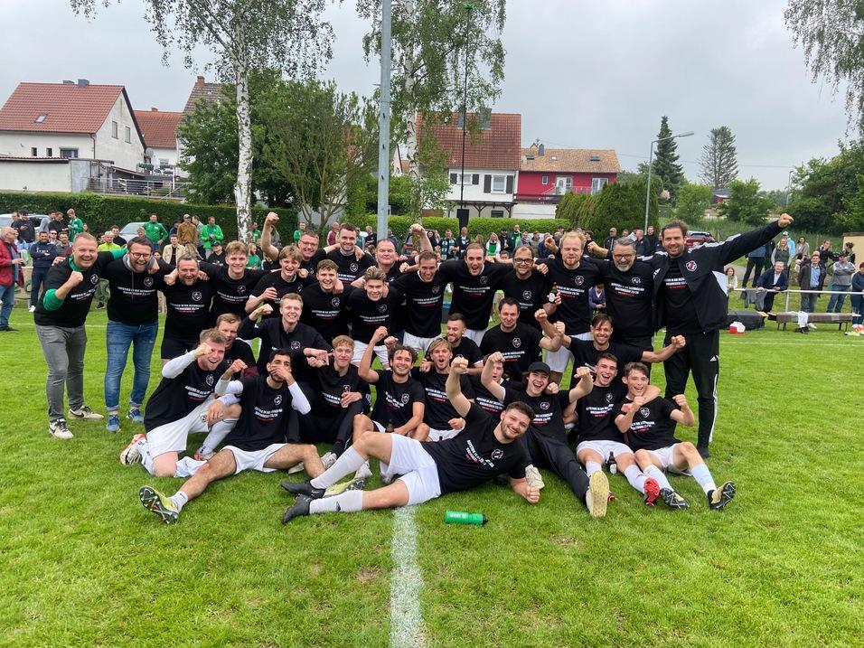 Gruppennahaufnahme von jubelnden Fußballspielern in schwarzen Trikots auf einem grünen Spielfeld nach einem Sieg.