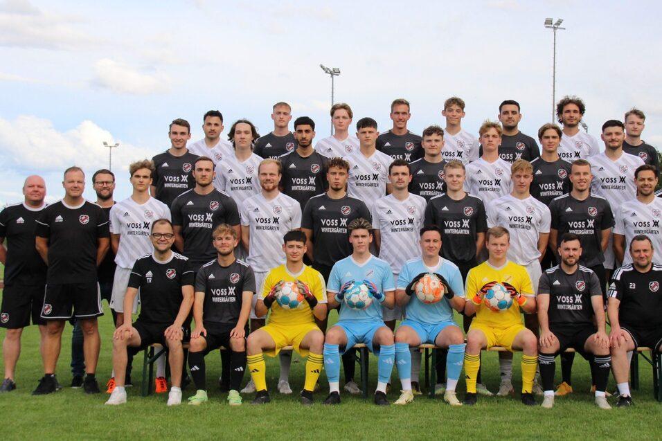 Mannschaftsfoto einer Fußballmannschaft mit Trainern, Spielern in Trikots und Torwarten auf einem Sportplatz.